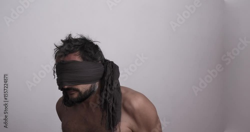 A bare-chested, blindfolded, unshaven man shaking with fear. Close-up
