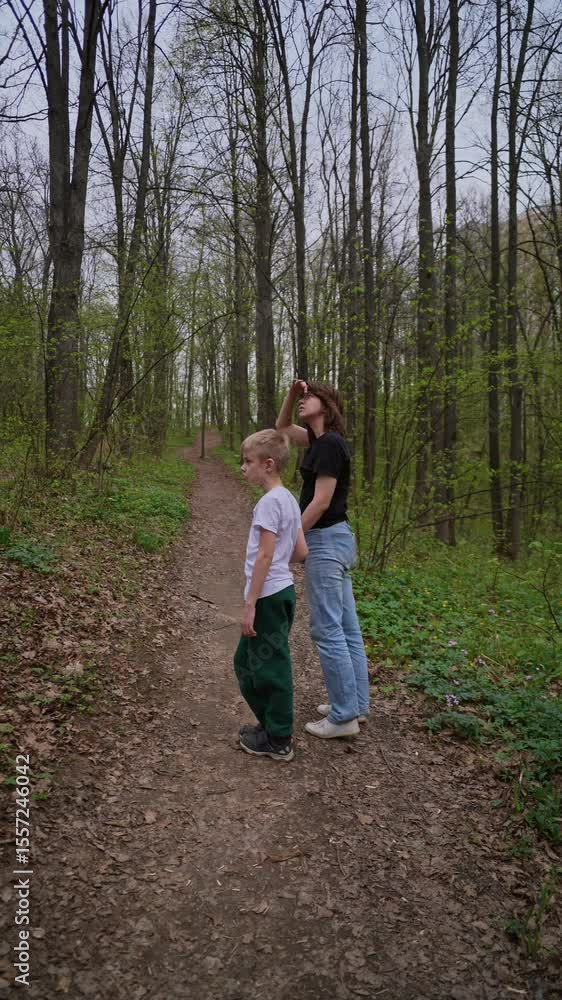 A mother and her son with a hearing aid enjoy a peaceful forest walk, sharing a genuine moment of connection and rehabilitation in nature. Authentic, heartwarming family bonding A mother and her son with a hearing aid enjoy a peaceful forest walk, sharing a genuine moment of connection and rehabilitation in nature. Authentic, heartwarming family bonding