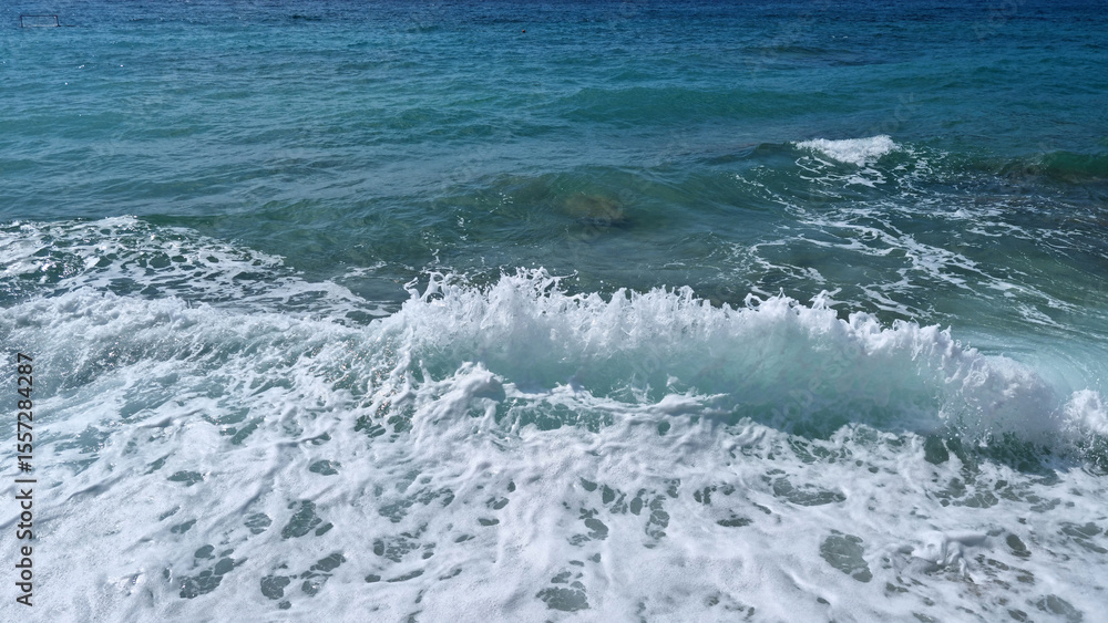 Fototapeta premium A view from Vela plaza in Baska of the turquoise sea with waves and Velebit and Prvic island in the distance