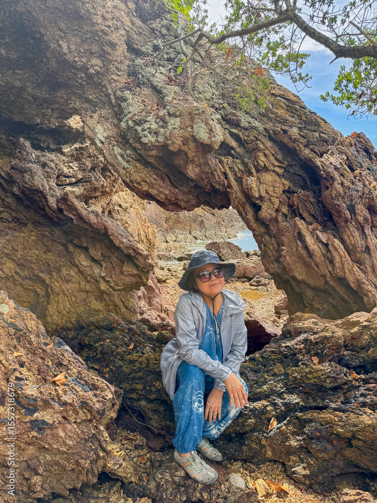 Naklejka premium Happy asian Thai elder woman standing in front of beautiful rock and beach view in Thailand.