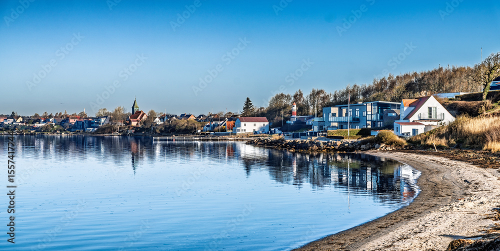 Obraz premium Scenic Coastal Town With Reflections Over Calm Water Under Clear Sky, Rendbjerg, Denmark