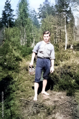 Vintage portrait of a young guy walking barefoot in the forest holding sneakers in his hands. Retro photo from 1962.