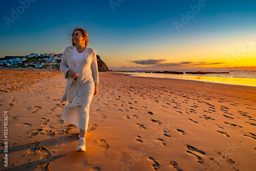 Beautiful mid adult woman enjoying walk on sandy beach on sunset on windy spring day. Front view. Monte Clerigo beach on Algarve coast in Portugal	
