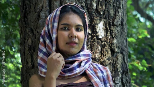 Young Asian woman smiling with Thai loincloth covers head standing near a big tree in the forest, portrait, close up