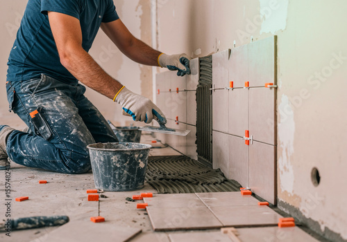 Construction worker laying ceramic tiles on a wall using adhesive and spacers during renovation