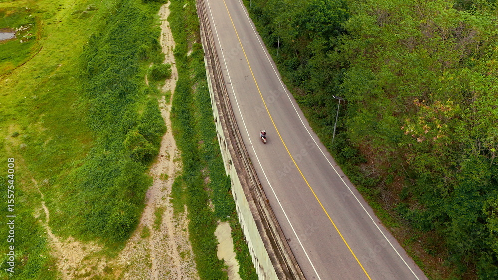 Fototapeta premium Aerial view of a road in the middle of the forest. Top view of asphalt road through forest with car adventure. Healthy environment road trip travel. 