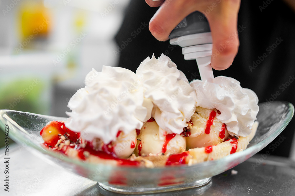 custom made wallpaper toronto digitalHand adding whipped cream to a banana split dessert with vanilla ice cream, strawberry sauce, and nuts in a glass dish. Tasty summer treat in preparation.