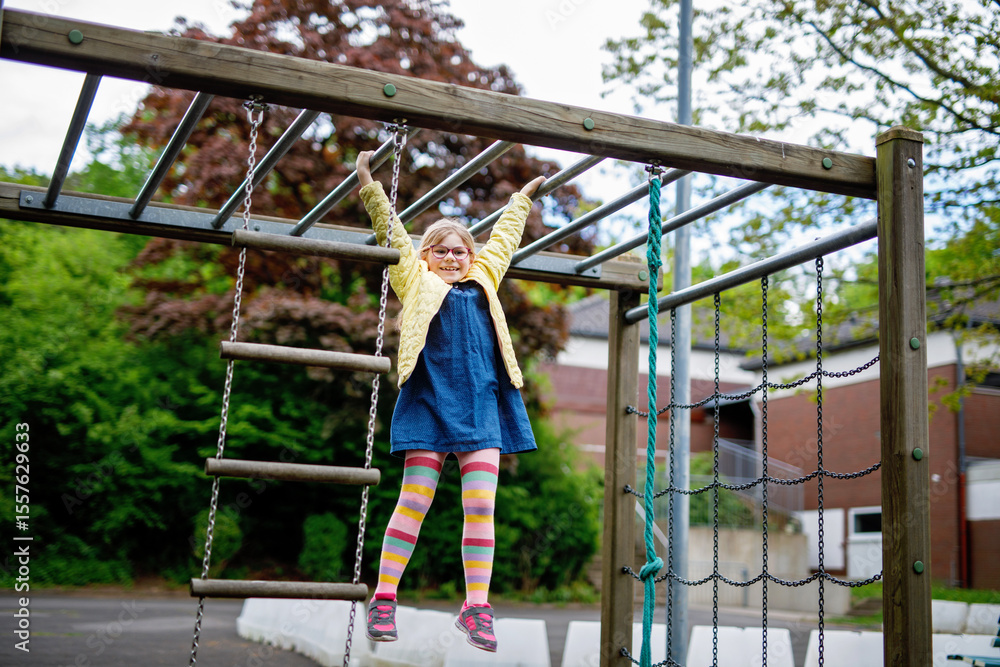 Obraz premium Little girl doing gymnastics on a climbing frame, horizontal bar on school yard. Child enjoying school break.