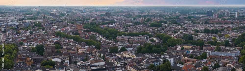Naklejka premium Aerial view of Utrecht, Netherlands, featuring the Dom Tower, a brick water tower, traditional Dutch architecture, and a flat horizon under a colorful sky.