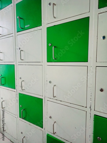 A grid of metal storage lockers in a repeating pattern. The doors are painted an alternating pattern of bright green and white, each featuring a small silver handle and a key lock. The photo shows the