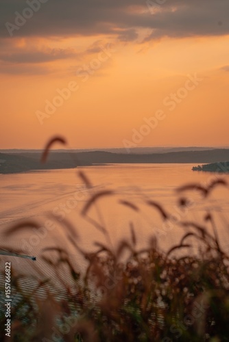 Tranquil Lake Sunset with Blurred Grass in Foreground and Orange Sky