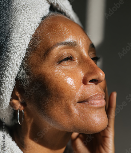 Smiling senior black woman applying moisturizing cream on face