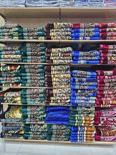 Shelves filled with neatly folded, colorful prayer rugs in a retail store, showcasing a variety of patterns and textures for religious practices.