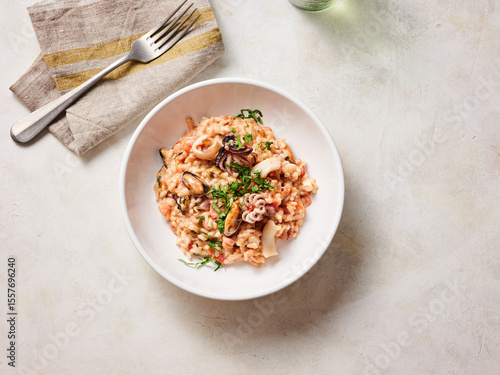 Creamy seafood risotto is artfully presented in a white bowl, showcasing shrimp and squid surrounded by fragrant herbs, perfect for a comforting meal