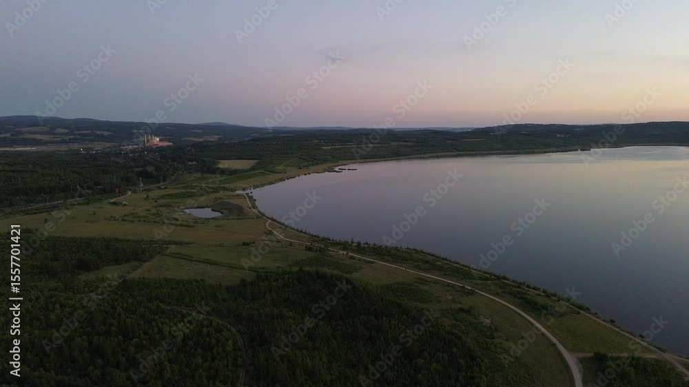 This sweeping aerial shot presents a wide view of Jezero Medard in Svatava at twilight, showcasing its long, curving shoreline bordered by lush forests and open fields. This sweeping aerial shot presents a wide view of Jezero Medard in Svatava at twilight, showcasing its long, curving shoreline bordered by lush forests and open fields.