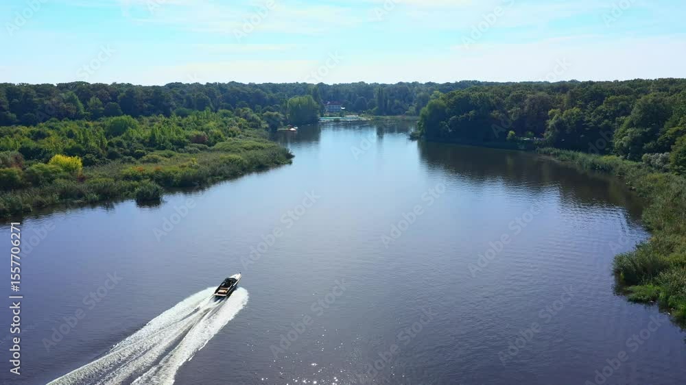 A boat cruises on a tranquil lake, surrounded by forest. Sailing boat on the forest lake at sunset. Speedboat filmed from drone on Snagov lake at sunset.Lens flare, Aerial drone shot. A boat cruises on a tranquil lake, surrounded by forest. Sailing boat on the forest lake at sunset. Speedboat filmed from drone on Snagov lake at sunset.Lens flare, Aerial drone shot.
