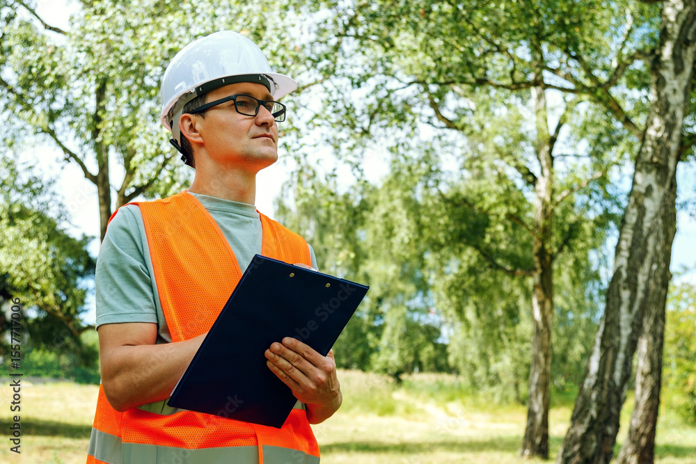 Fototapeta premium Environmental engineer man in the forest notes the ecological situation. Ecologist technician with a tablet checks the trees. Forester worker.