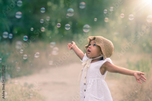 baby and soap bubbles. film photography. A little girl is waving her arms and trying to catch a lot of soap bubbles