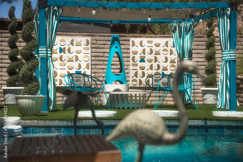 Outdoor estate pool scene with brass sculptural birds in the foreground, mid-century seating in the background, and spiral trees surrounding the space. Artful and serene.
