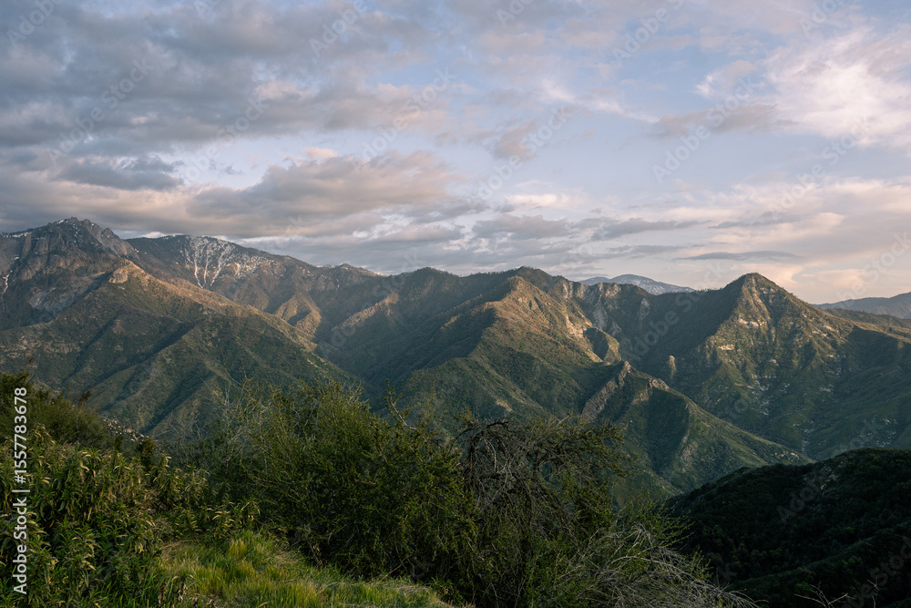 Fototapeta premium Pastel-toned panorama of coastal range, late-day clouds casting soft shadows over folded ridges and remote canyons. 