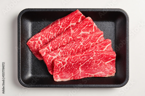 Top view studio photo of raw frozen wagyu beef slices arranged on a black food tray. The meat features beautiful marbling, highlighting the high quality and tenderness of premium wagyu.