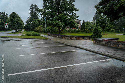 Wallpaper Mural An empty, wet parking lot on a rainy day, with sidewalks, green trees, traffic signs, and a residential building in the background. Overcast sky and copy space. Torontodigital.ca
