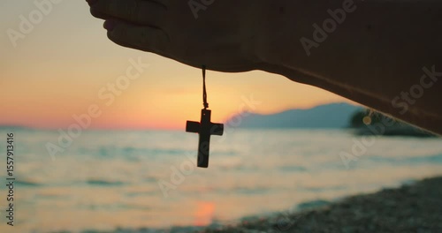 Wallpaper Mural Hand holding a wooden cross necklace in front of the sea during peaceful sunset Torontodigital.ca