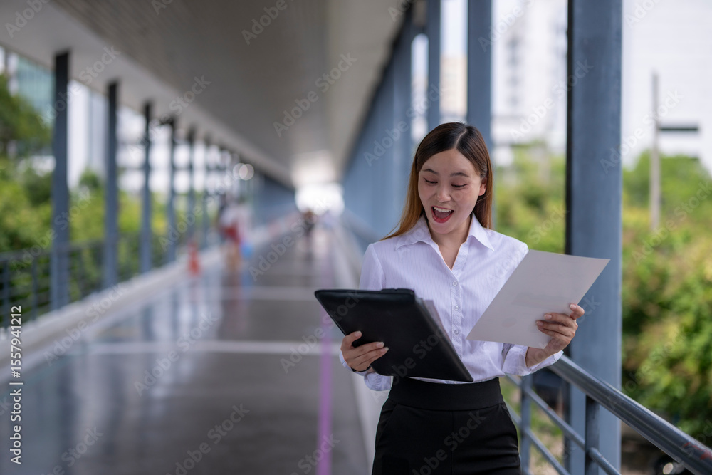 Excited businesswoman celebrating success while reading documents in a modern urban setting Excited businesswoman celebrating success while reading documents in a modern urban setting