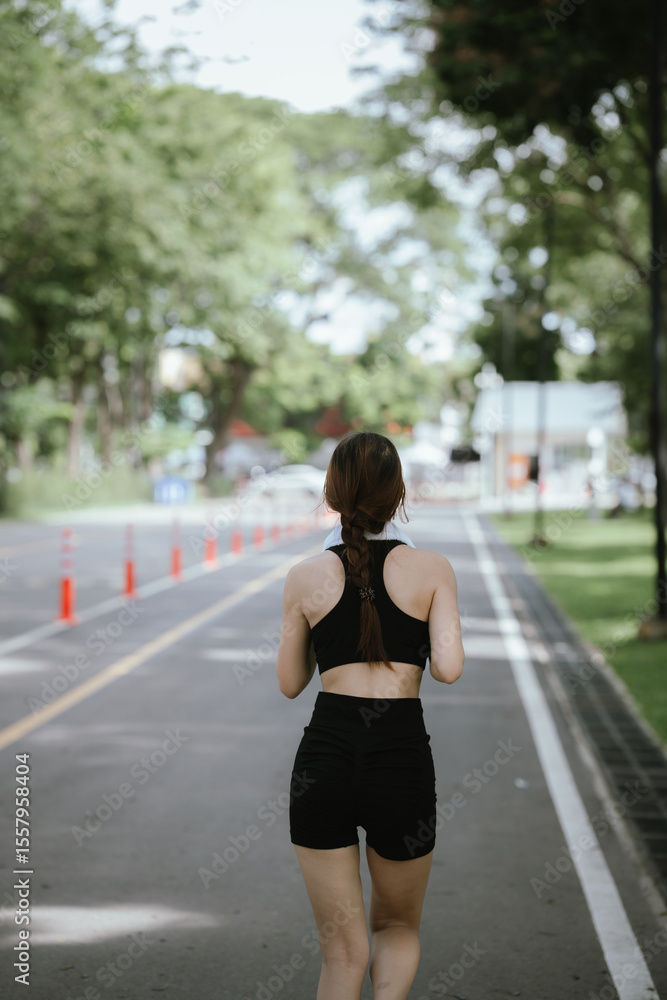 A young woman is jogging outdoors in a park, wearing workout clothes. She is surrounded by nature and sunlight. She enjoys exercise, fresh air, energy and healthy living. A young woman is jogging outdoors in a park, wearing workout clothes. She is surrounded by nature and sunlight. She enjoys exercise, fresh air, energy and healthy living.