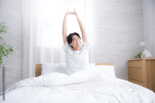 Konstfotografi 朝日を浴びるベッドで寝起きの若い男性　腕を伸ばしストレッチをする