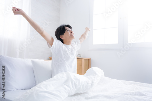 Konstfotografi 朝日を浴びるベッドで寝起きの若い男性　腕を伸ばしストレッチをする　バンザイのポーズ