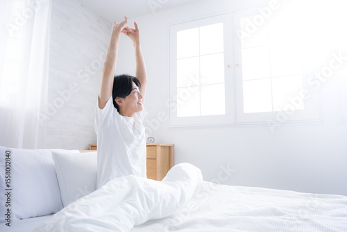 Wallpaper Mural 朝日を浴びるベッドで寝起きの若い男性　腕を伸ばしストレッチをする Torontodigital.ca