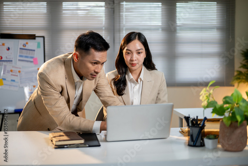 Obraz na plátně Asian businessman looking closely at female coworker's laptop screen on working table in the office