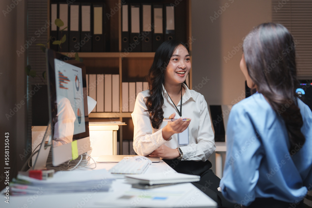 Obraz premium Two businesswomen discussing charts on computer in office at night