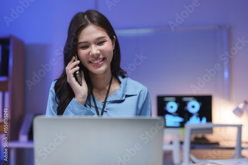 Asian businesswoman talking on phone and working on laptop at night