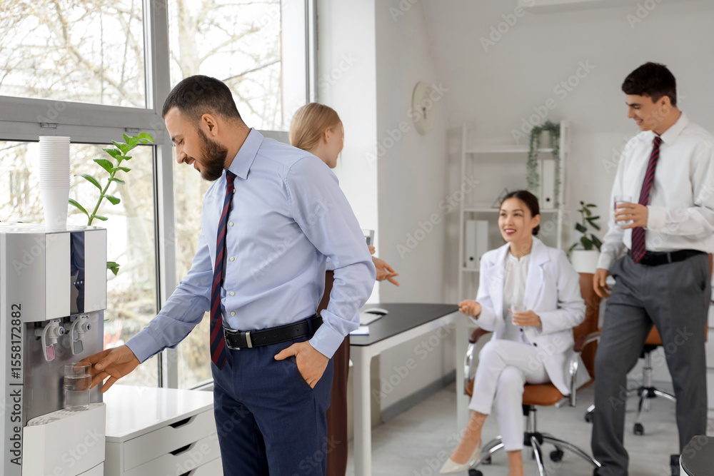 Obraz premium Young businessman pouring water from cooler in office