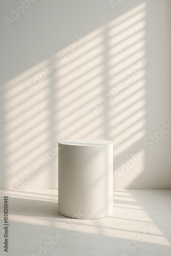 Cylinder pedestal in warm sunlight with soft blind shadows on cream wall