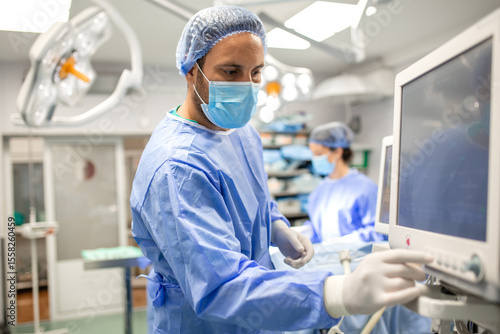 Anesthesiologist monitoring patient vital parameters on a digital screen during surgery. Focused doctor adjusting settings on anesthesia equipment to maintain patient stability in the operating room
