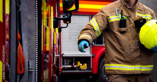 Firefighter in action with hand reaching for fire truck door. An emergency services fireman and two fire engine appliances as smoke billows through the air.
