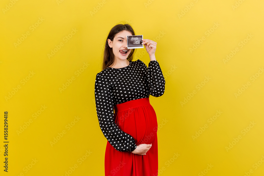 Obraz premium Cute Pregnant Lady Posing With Baby Sonography Photo Near Colored background. Concept of pregnancy, gynecology, medical test, maternal health