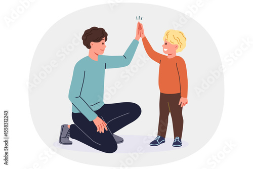 Father supports young son by high-fiving boy and raising child on own after divorce from mother. Young single dad smiles while communicating with son, celebrating father family day
