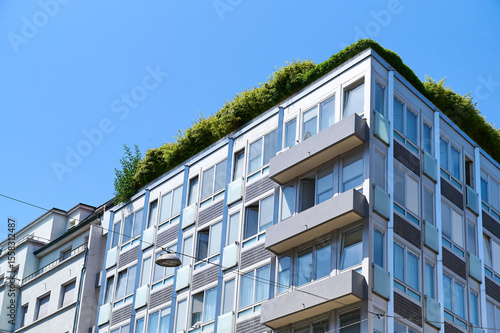 A contemporary building features lush rooftop gardens against a vibrant blue sky, showcasing urban greenery.