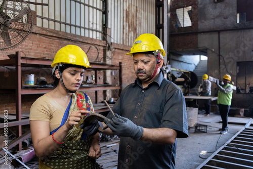 Two indian engineers wearing safety hard hat and discussing work at industrial factory, skill india concept.