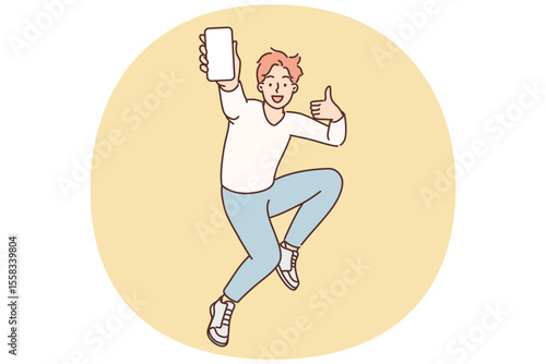 Encouraged man jumps up with mobile phone in hands showing blank screen gadget and shows thumbs up