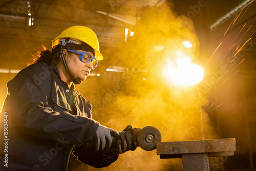 Side view portrait of mature female worker cutting metal at industrial plant.