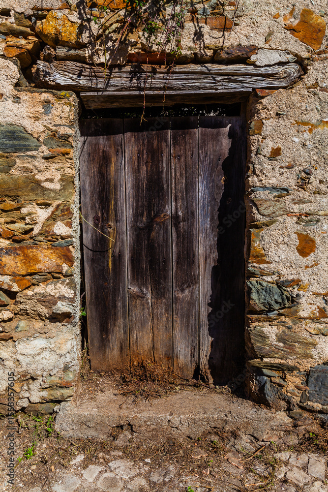 Fototapeta premium A weathered wooden door set in a stone wall stands under sunlight