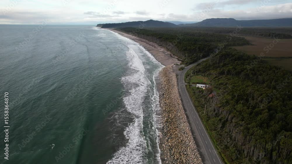 Coastal Road Winding Through Dense Forest Along Rugged Shoreline Of Maori Beach On Bruce Bay In New Zealand. aerial shot Coastal Road Winding Through Dense Forest Along Rugged Shoreline Of Maori Beach On Bruce Bay In New Zealand. aerial shot