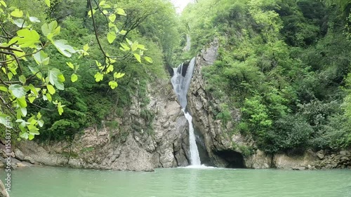 Still greenish-blue lake framed by trees and cliffs in peaceful mountain forest.