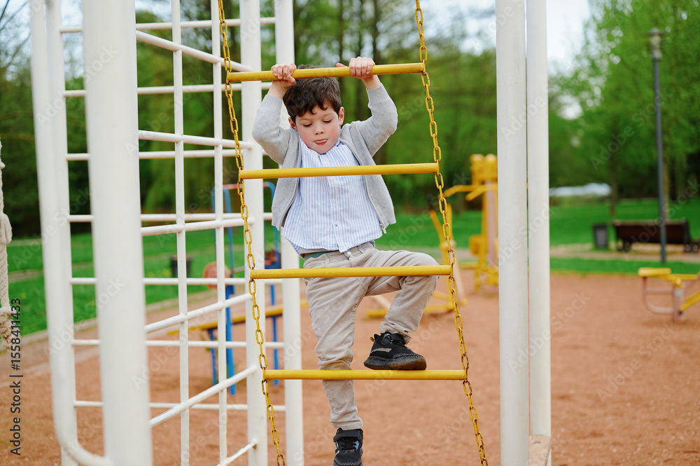 Obraz premium child climbing playground equipment outdoors with determination and focus. active boy wearing casual attire explores jungle gym in park setting. childhood adventure and physical play