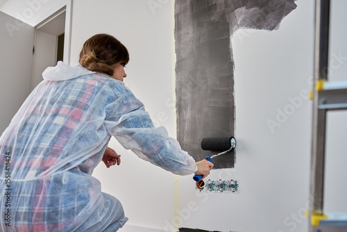 Quadro su tela Woman in protective suit pants white wall with black print using roller during renovation